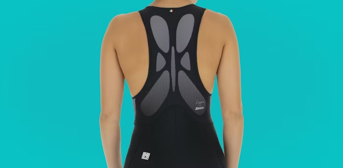 Back View of a Woman Wearing a Black Cycling Bib Shorts with Mesh Racerback Design on a Turquoise Background